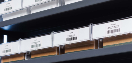 Close-up of a shelf containing small boxes with scannable barcode labels, organized in a storage system.