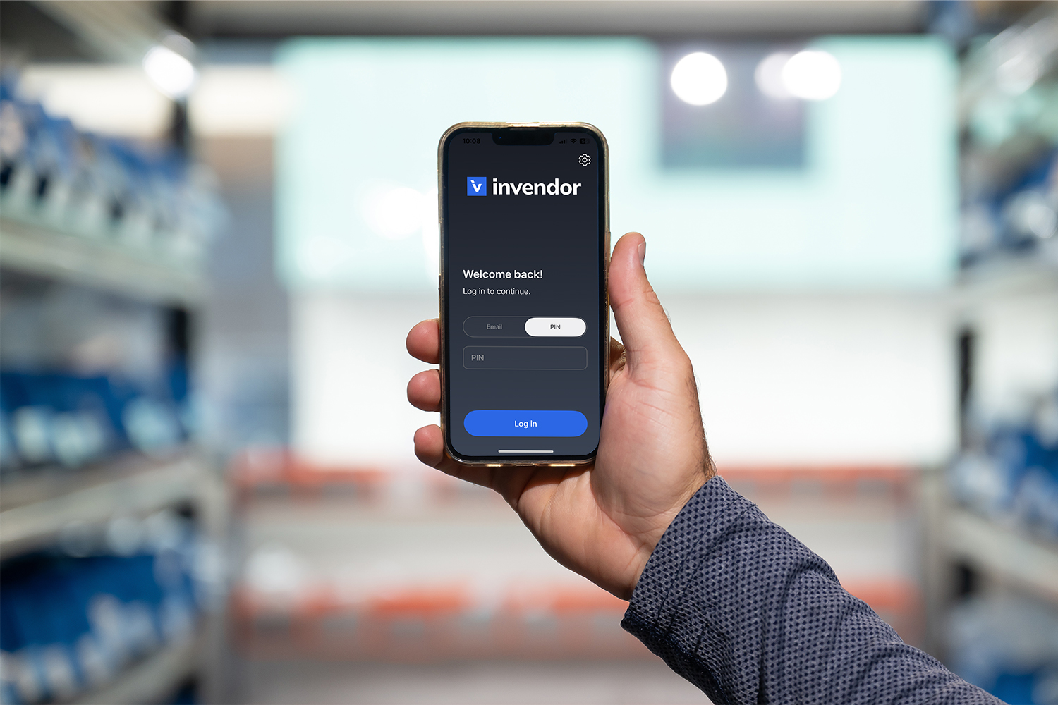 Hand holding a smartphone in an industrail setting, on the smartphone screen is Invendor's logo and login options.