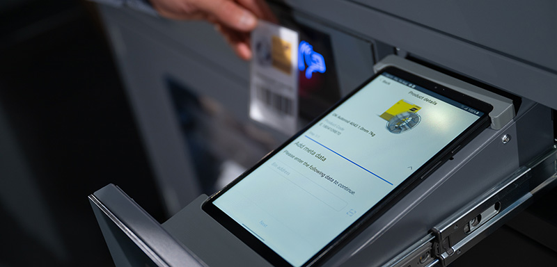 Tablet in a smart storage drawer displaying inventory details, with a hand scanning a barcode card nearby.