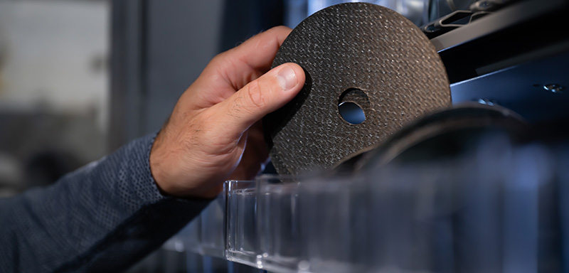 Close-up of a hand retrieving a circular abrasive disc from a storage compartment.