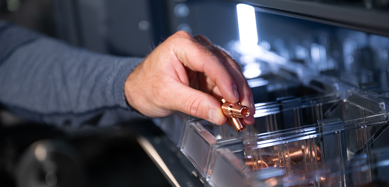 Close-up of a hand retrieving a copper nozzles from a storage compartment.