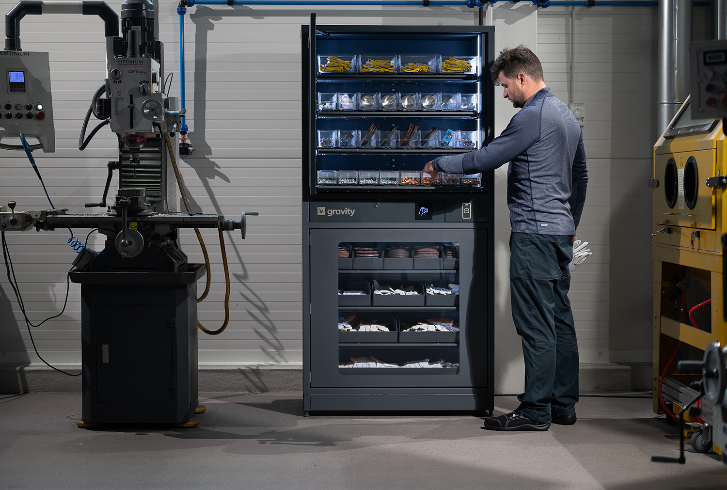 Man accessing items in a Gravity smart storage cabinet in an industrial workspace, surrounded by machinery and equipment.