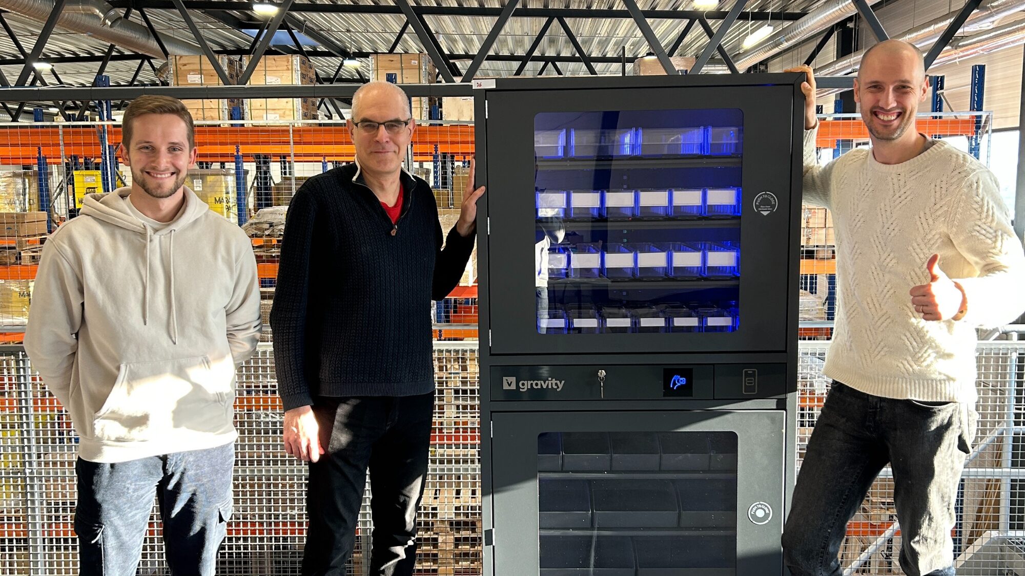 Three men standing next tothe industrial vending machine and smiling to the camera